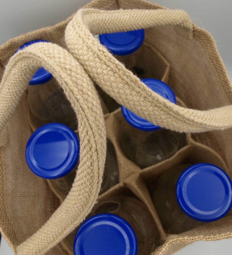 A jute bag filled with blue bottles of Handy 6 Bottle Carrier With Divider – Jute Syrups.